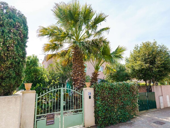 Una entrada protegida con una palmera y un edificio al fondo.