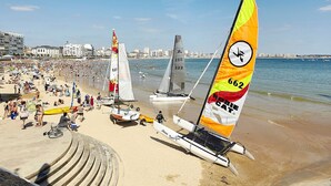 A beach with sailboats, a sandy shore, and buildings in the background. - Seaside studio with balcony, 50m from the beach (Les Sables-d'Olonne)