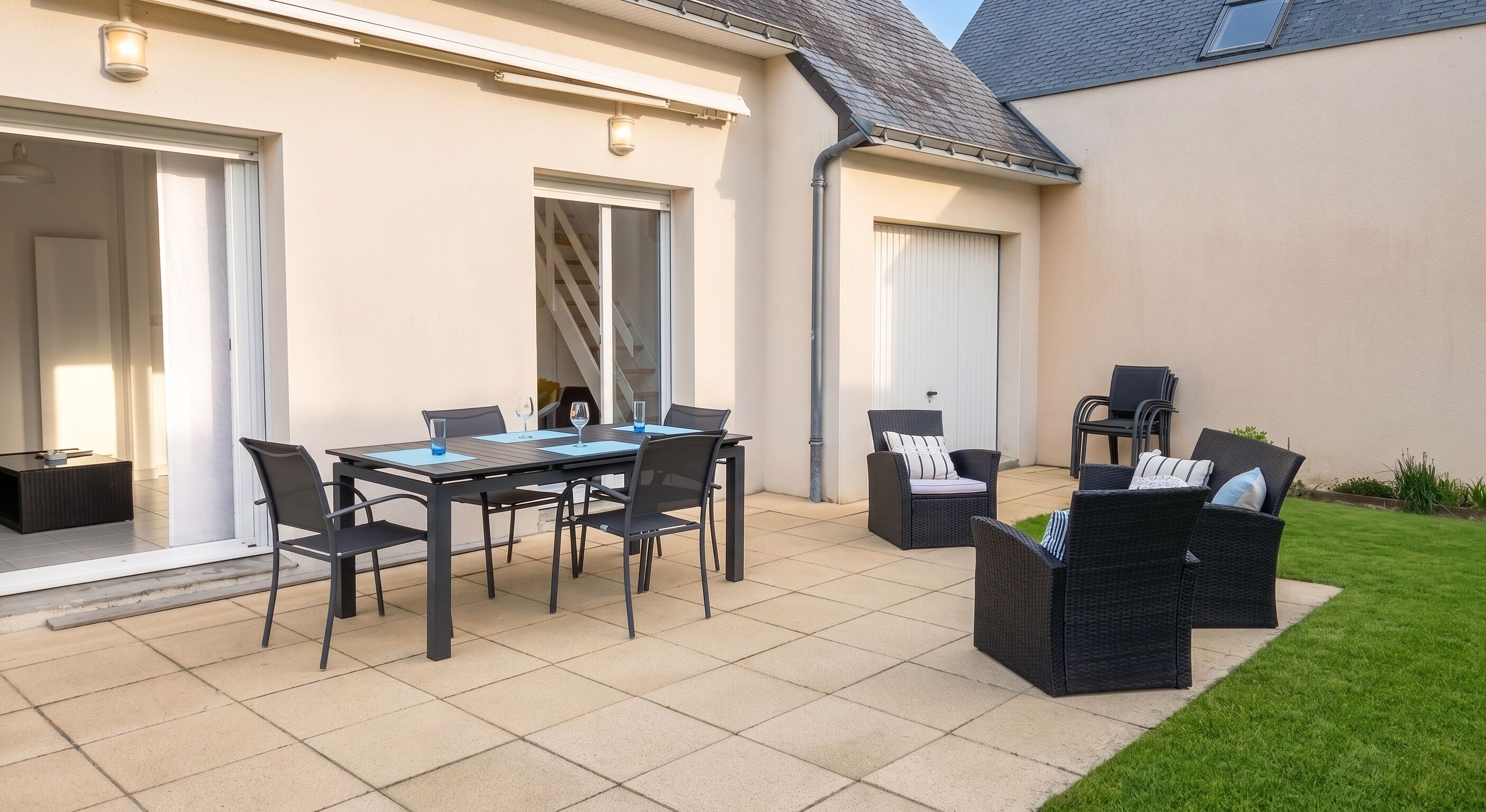 Een terras buiten met een eettafel en stoelen, een kleine tuin en een gebouw met een lichtgekleurde gevel.