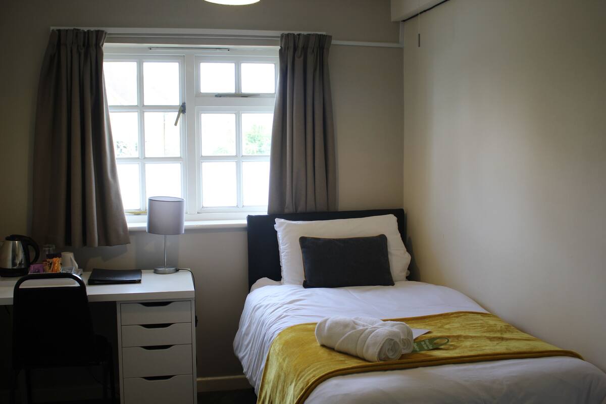 Quarto de hotel com cama, escrivaninha e janela com cortinas.