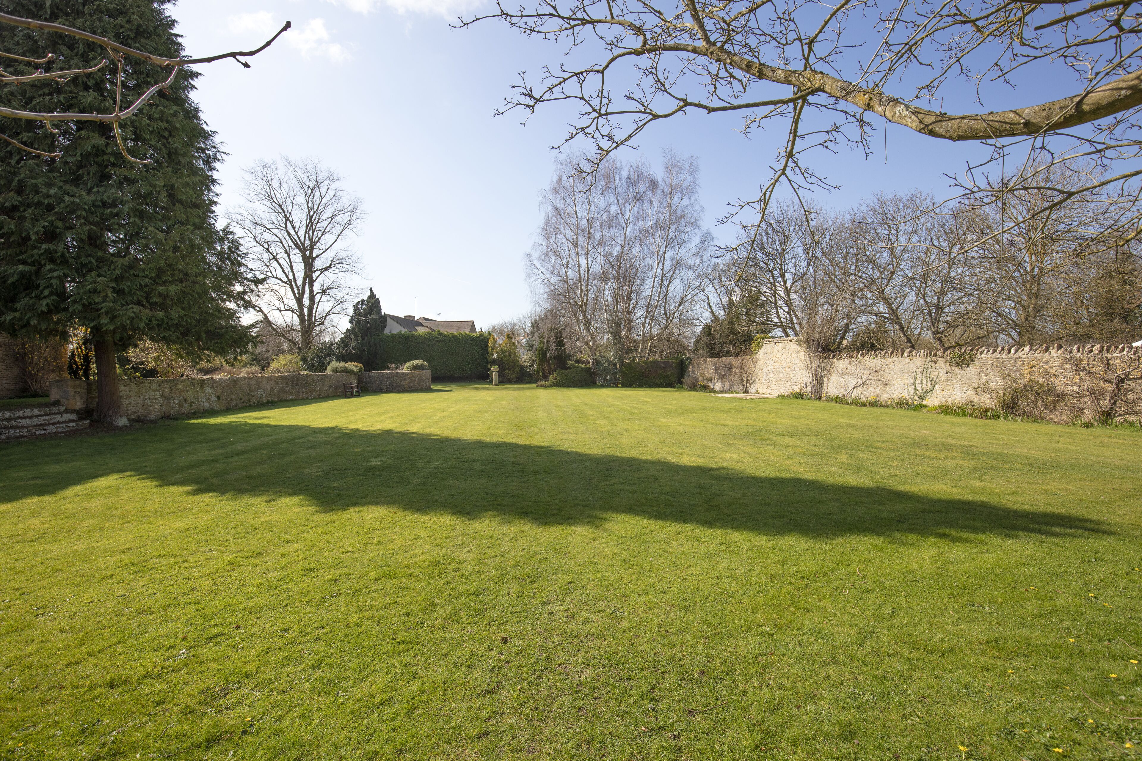 A well-maintained lawn with a stone wall and trees in the background.