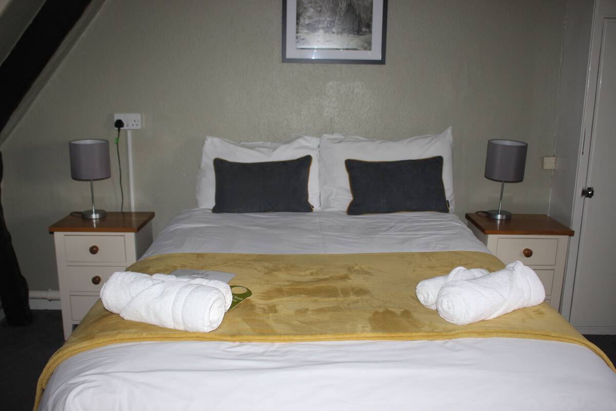 Quarto de hotel com uma cama, duas mesas de cabeceira, duas luminárias e um quadro na parede.