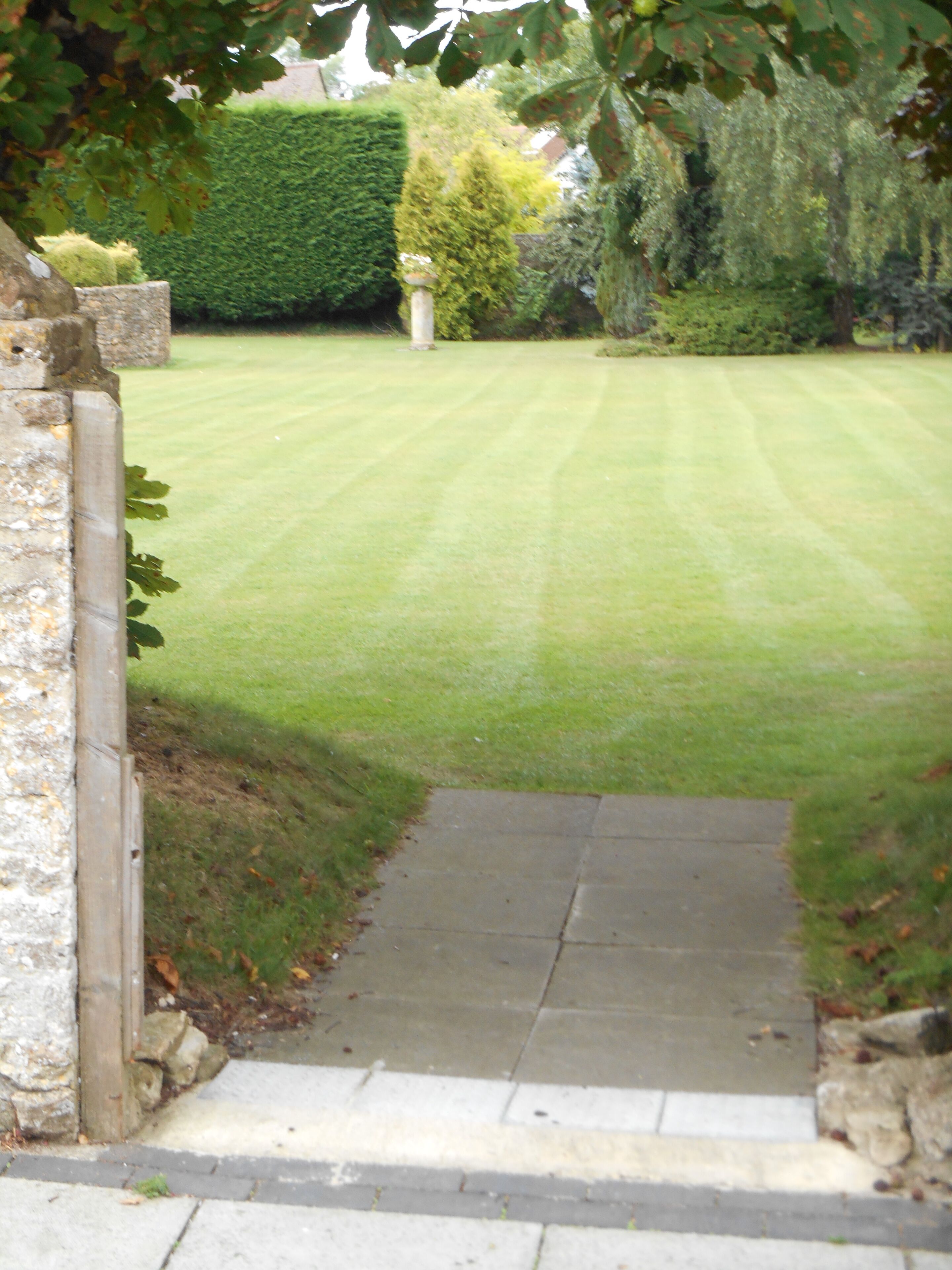 A pathway leading into a well-maintained garden with a neatly trimmed lawn and a hedge in the background.