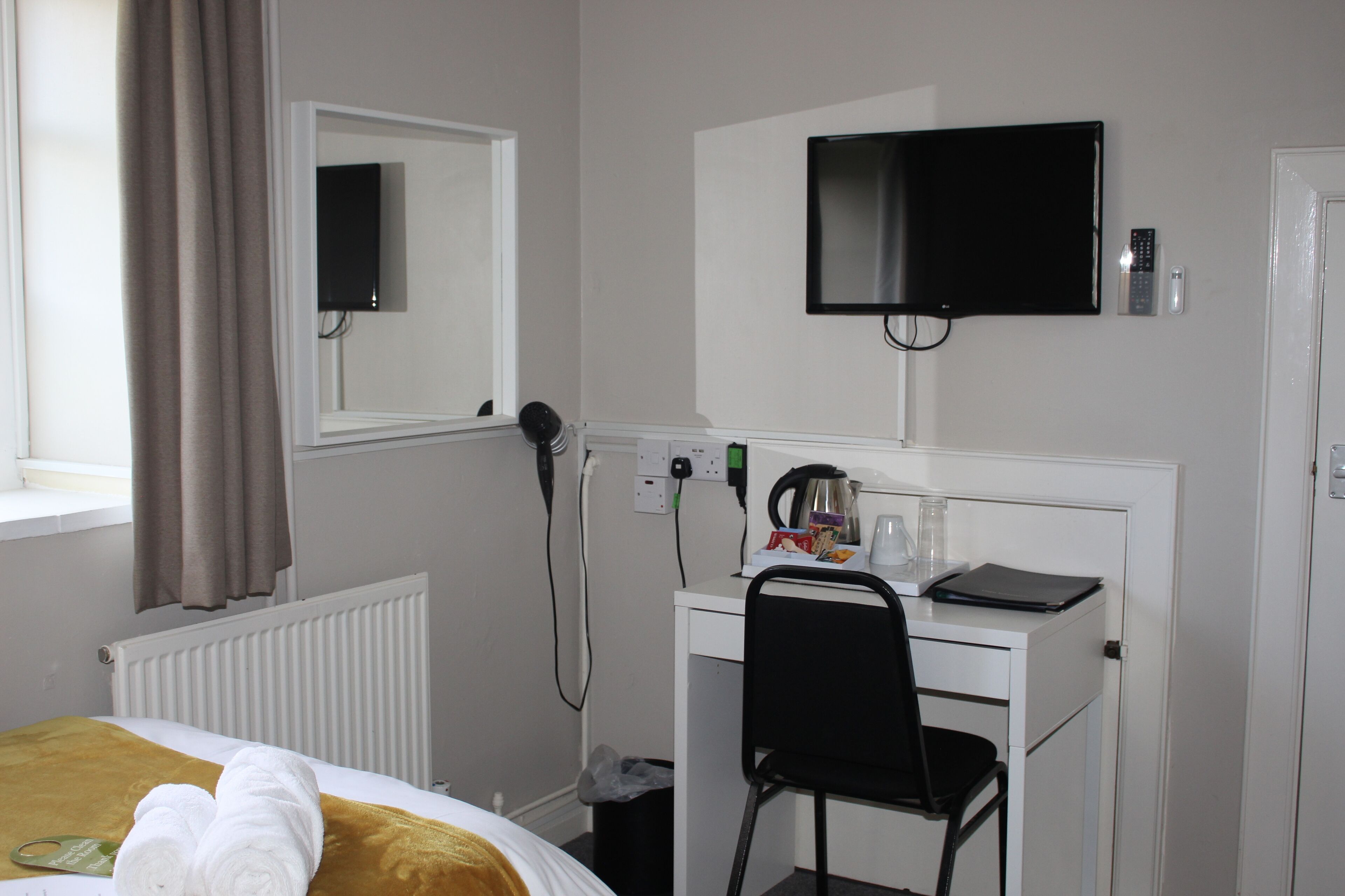 Une chambre d’hôtel avec un lit, un bureau et une chaise, une télévision et une fenêtre avec des rideaux.