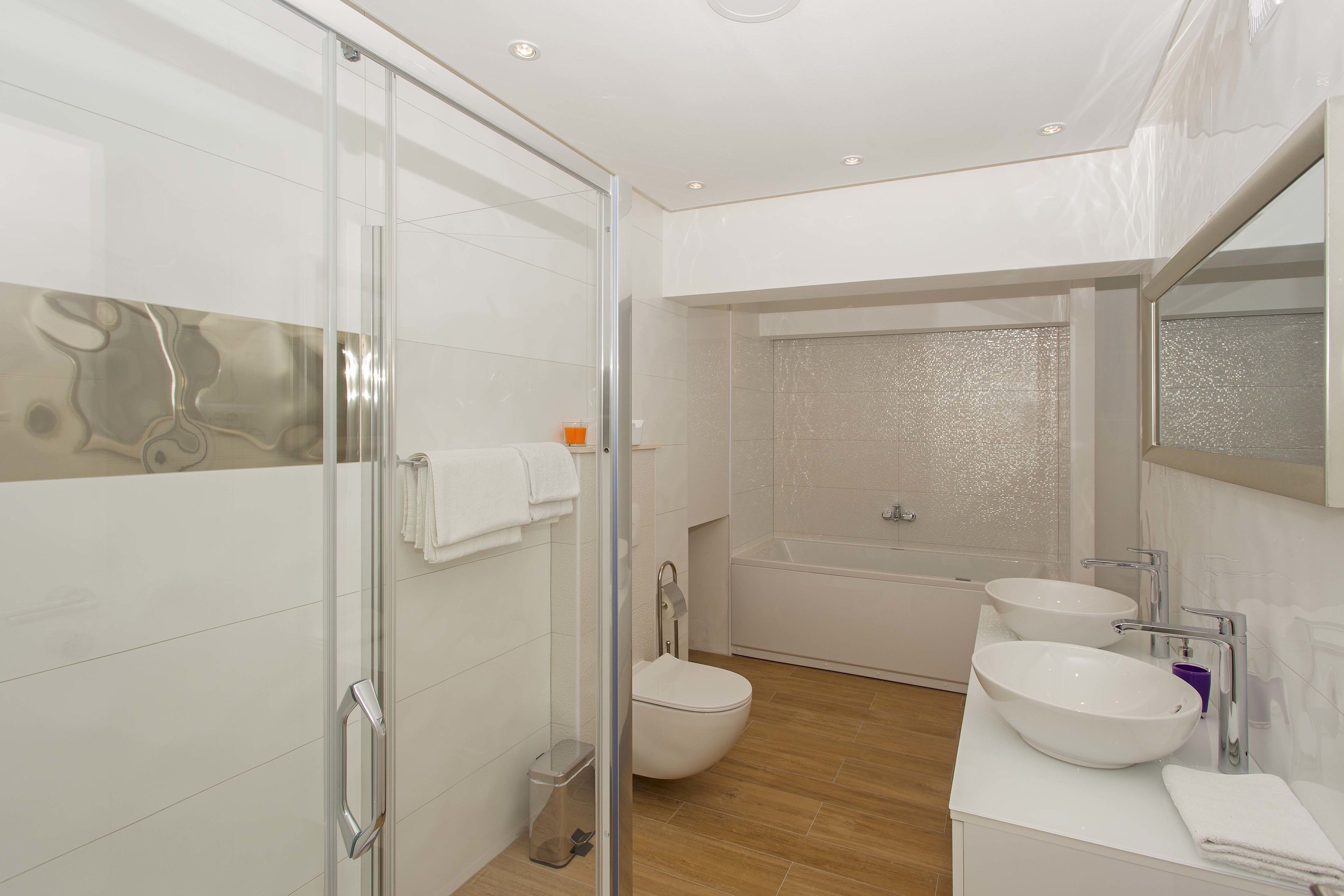 Ein modernes Badezimmer mit Duschkabine aus Glas, einer Badewanne und zwei Waschbecken.