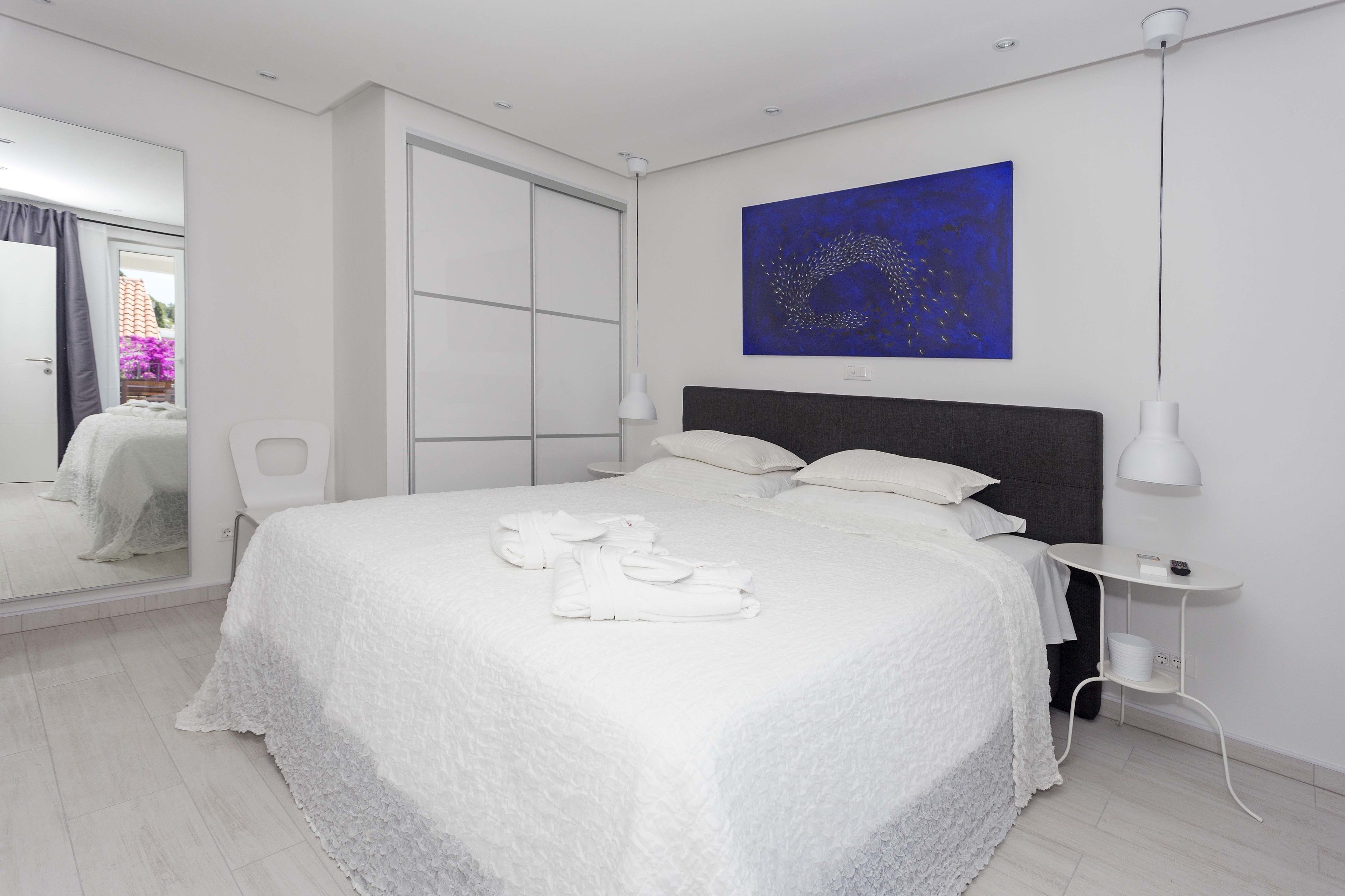 A modern bedroom with a large bed, a bedside table, a wall-mounted painting, and a mirror.