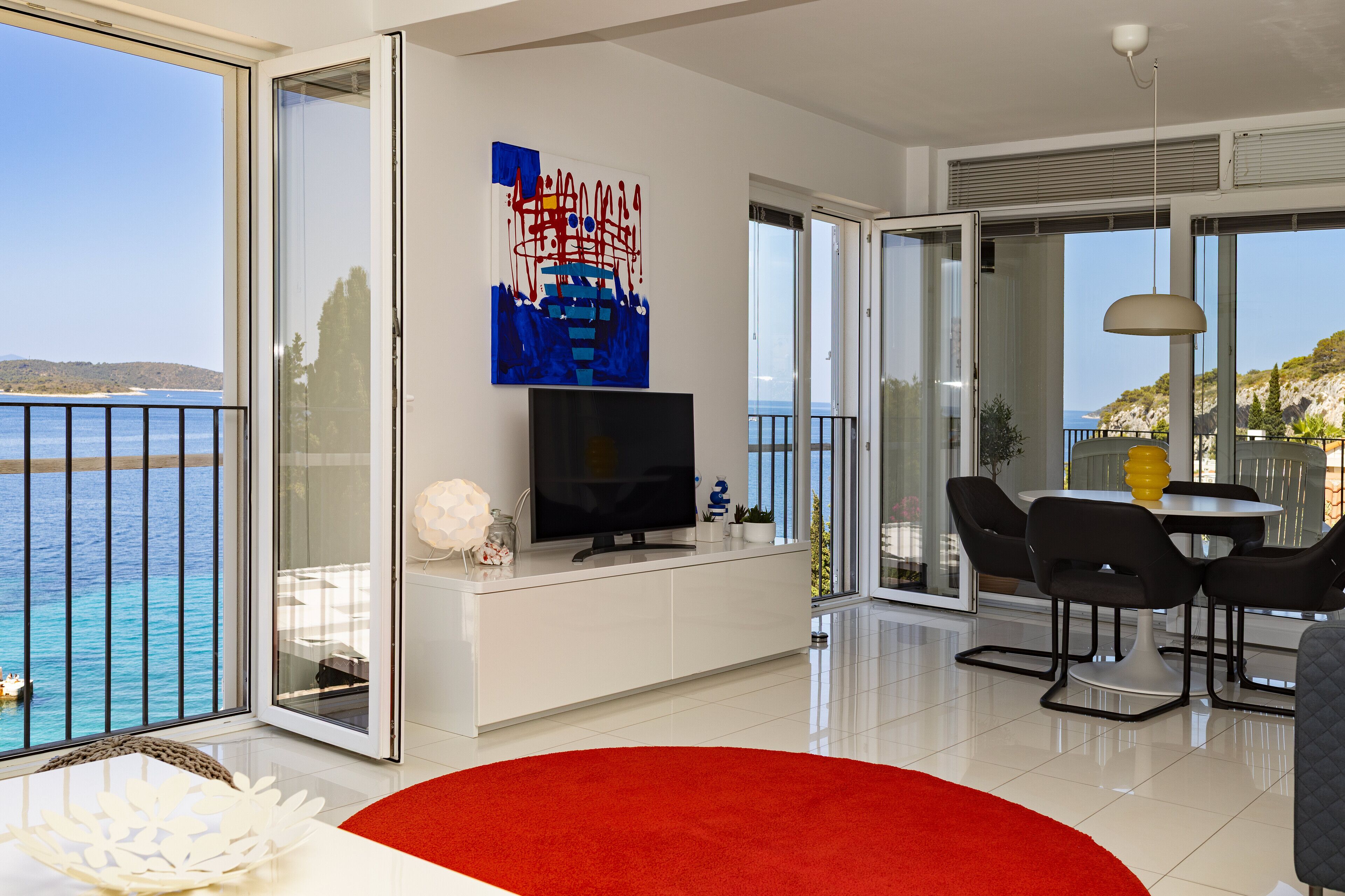 Uma sala de estar moderna com televisão, um tapete vermelho e um espaço de jantar com cadeiras e mesa.