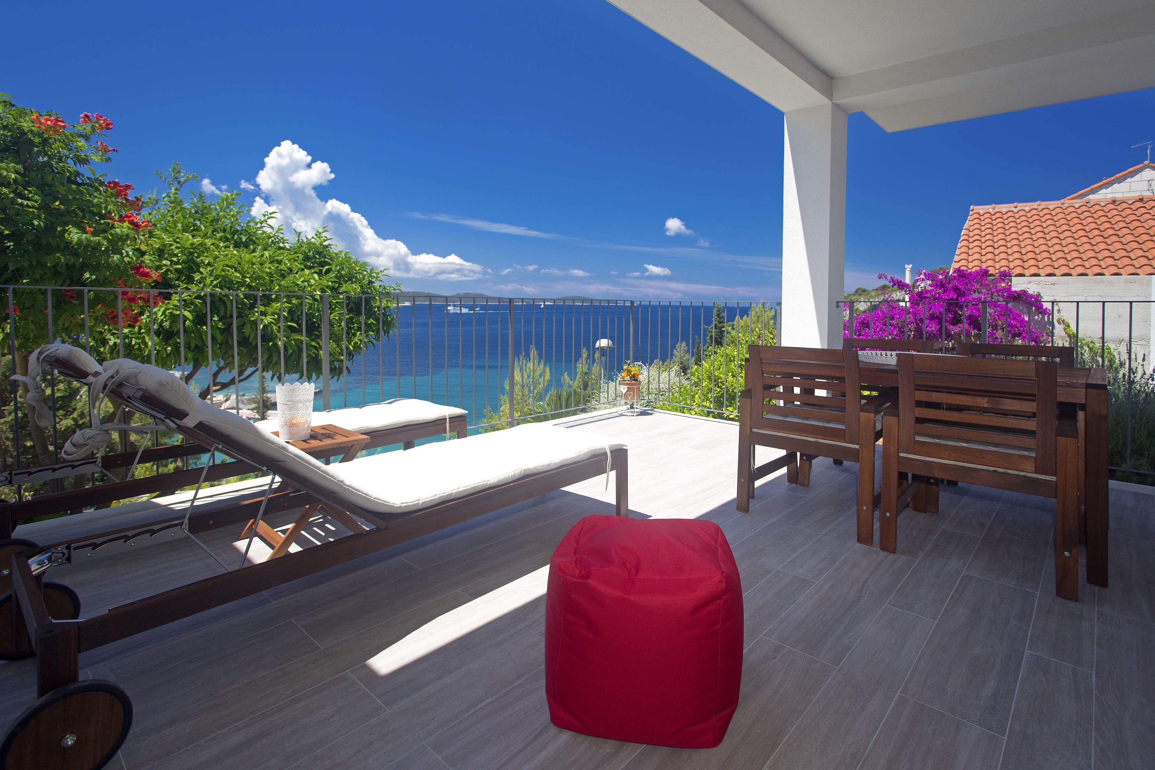 A balcony with a pool, wooden furniture, and a view of the sea.