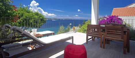 A balcony with a pool, wooden furniture, and a view of the sea.