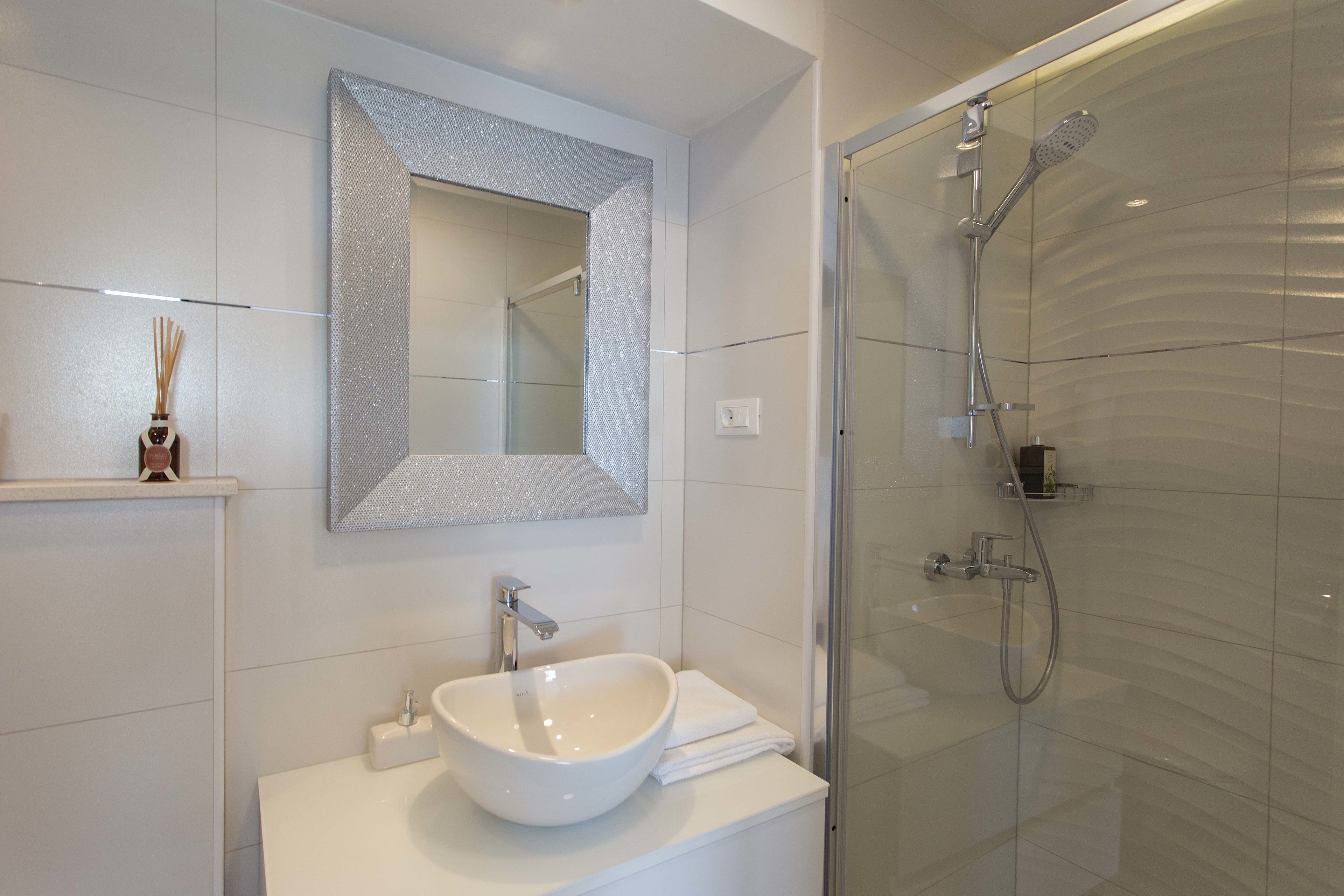 Une salle de bain moderne avec un grand miroir, un lavabo blanc et une douche à parois de verre.