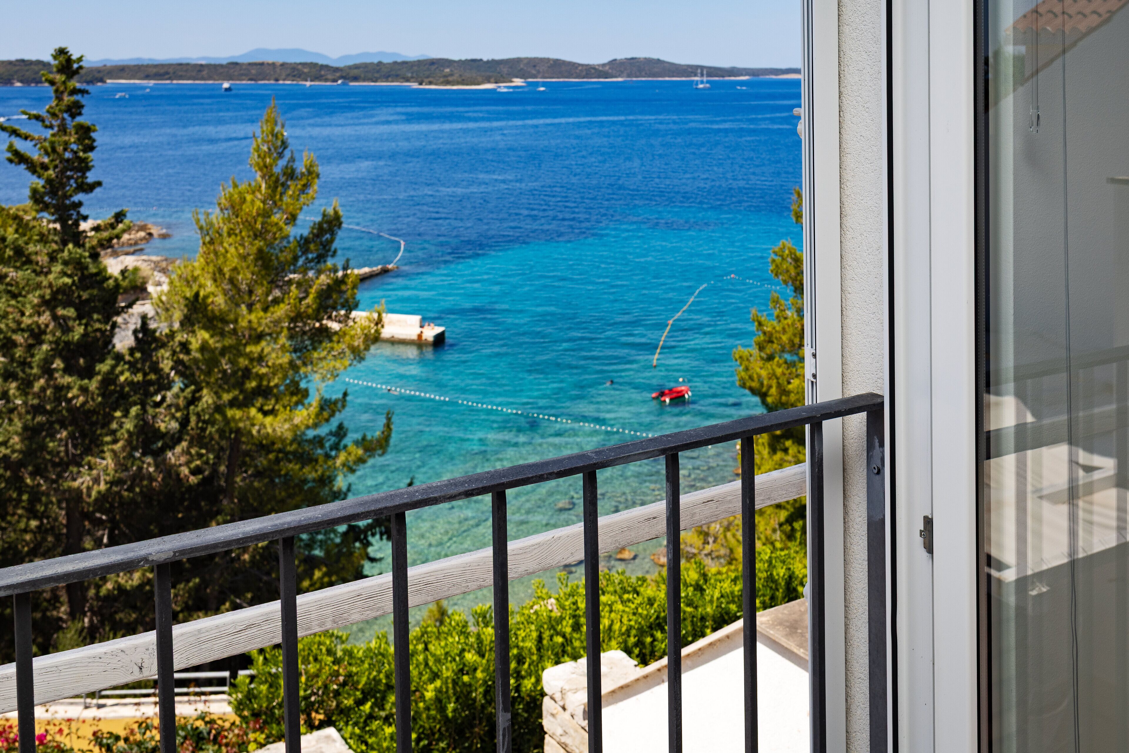 Un balcón con vistas despejadas a un mar turquesa, un barco rojo y vegetación circundante.