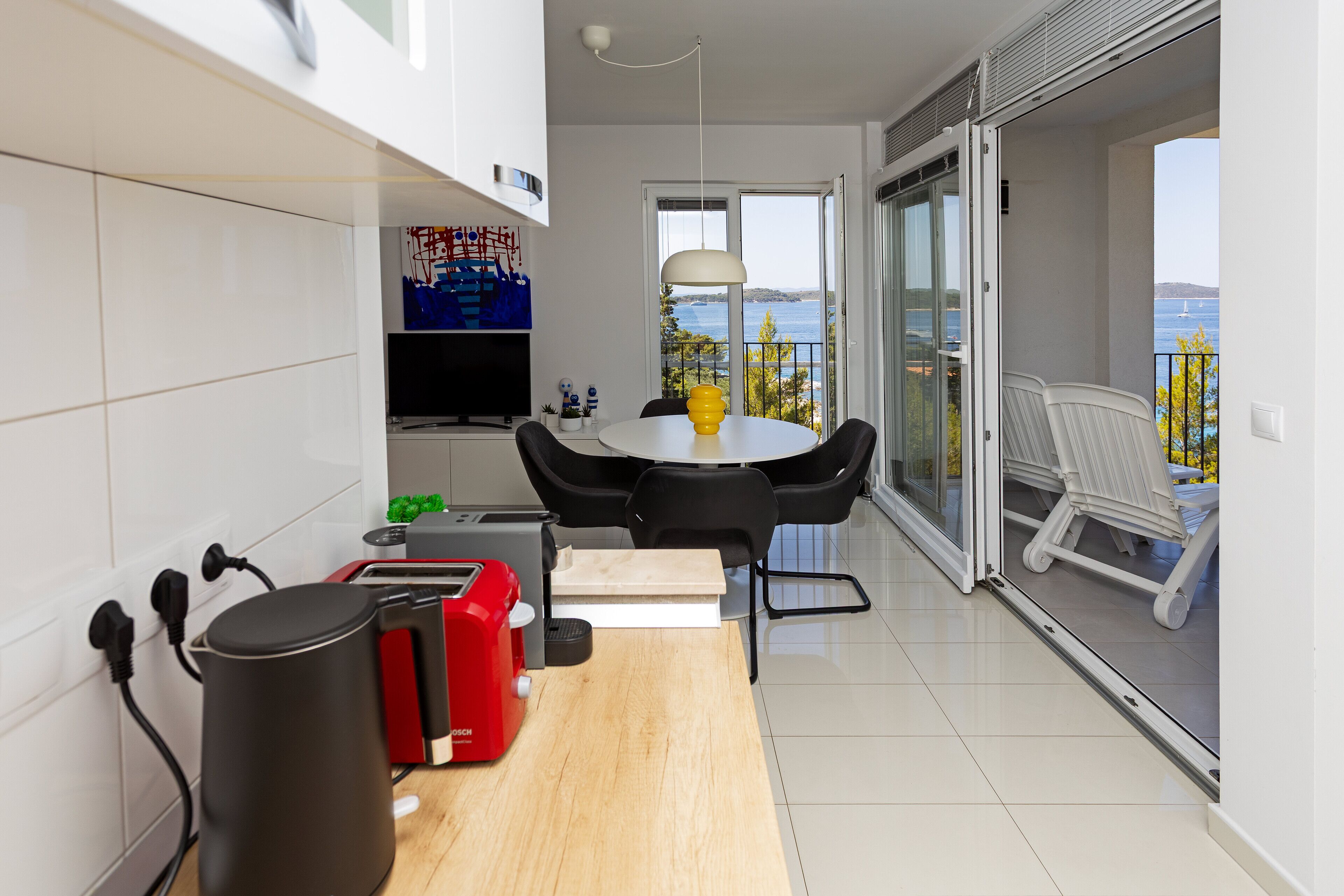 A modern kitchen with a dining area, a coffee machine, and a view of the sea.