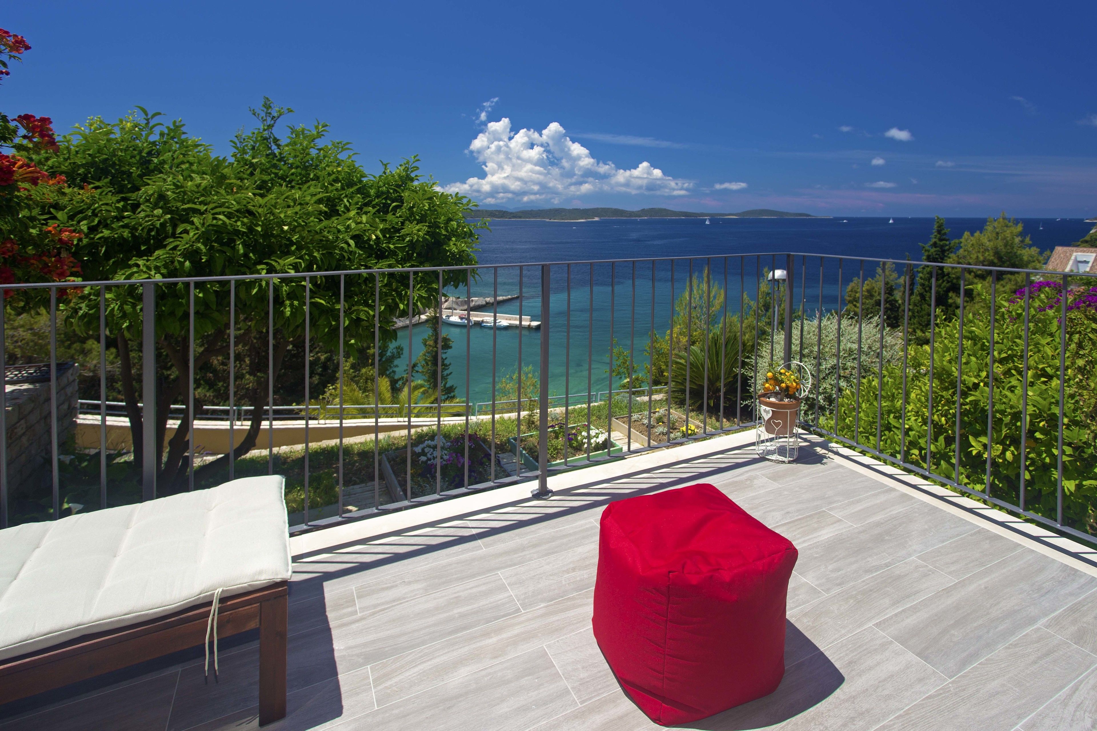 Un balcón con un sillón de mezcla de frijoles rojo, un banco acolchado blanco y vista al mar y a islas distantes.