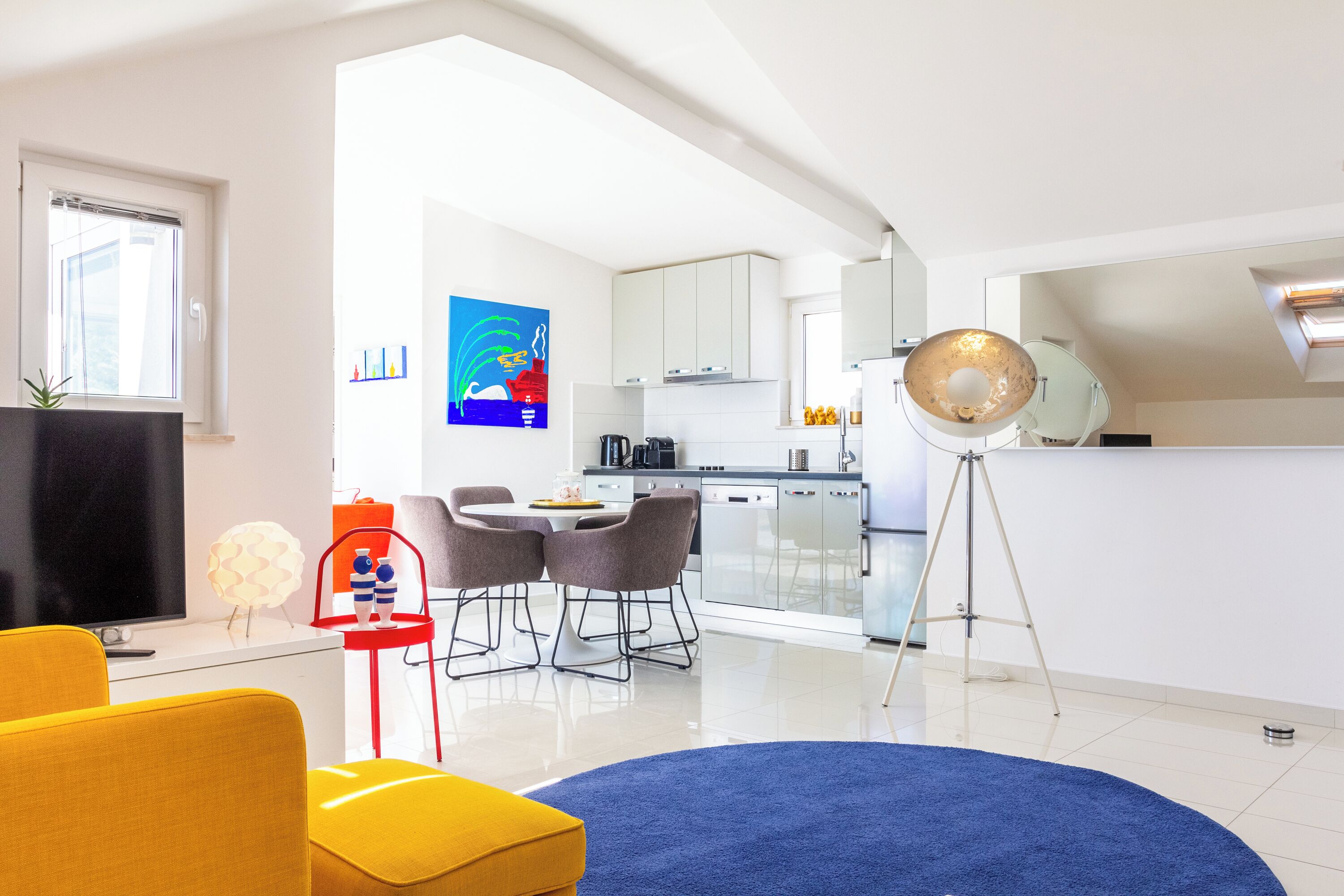 Een moderne woonkamer met een televisie, een gele bank en een eetgedeelte met een tafel en stoelen.