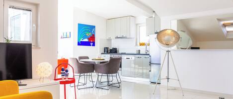 Una sala de estar moderna con televisor, sofá amarillo y un comedor con mesa y sillas.