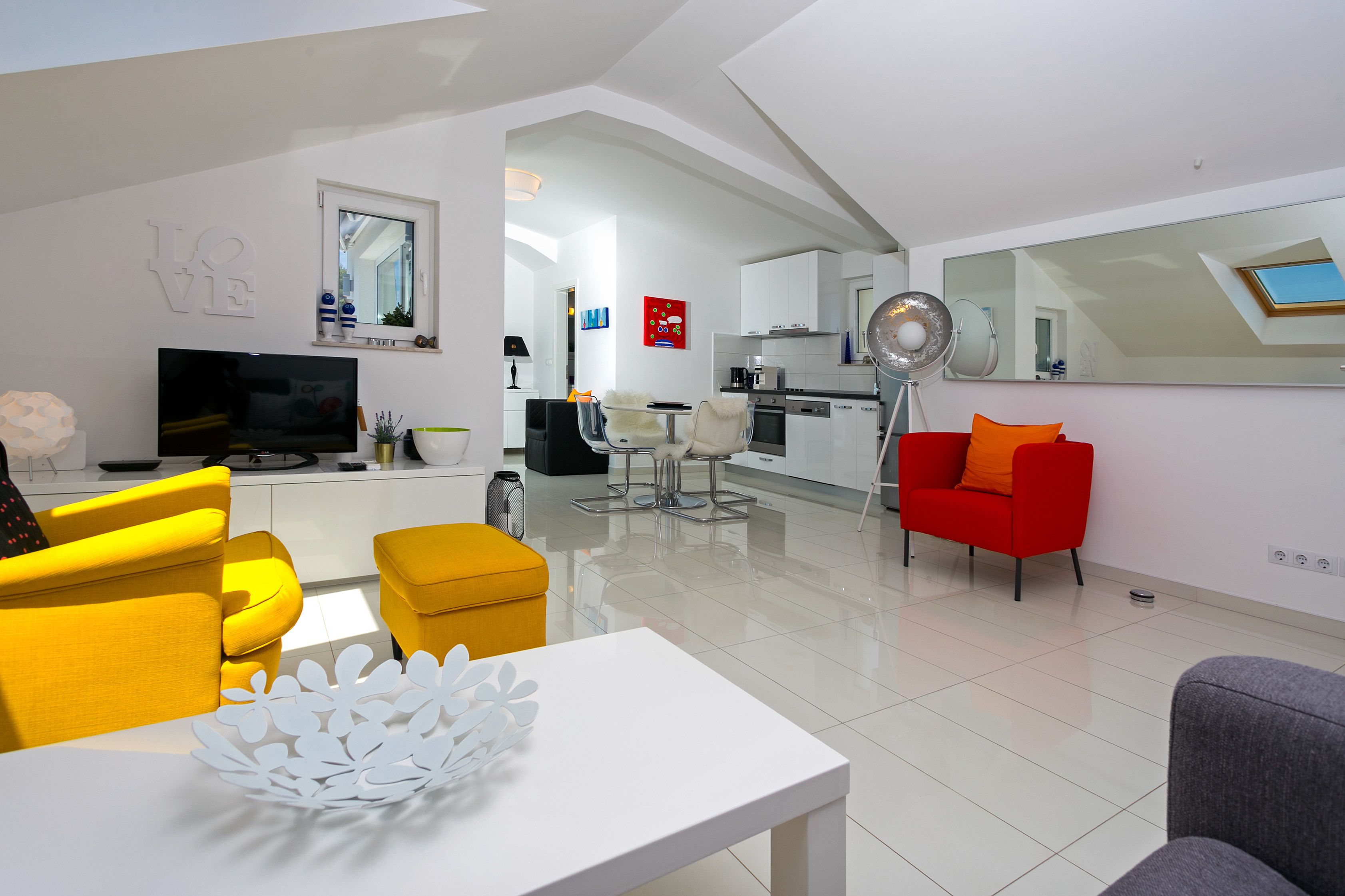 Una sala de estar moderna con sofás amarillos y grises, una mesa de centro blanca y un sillón rojo.