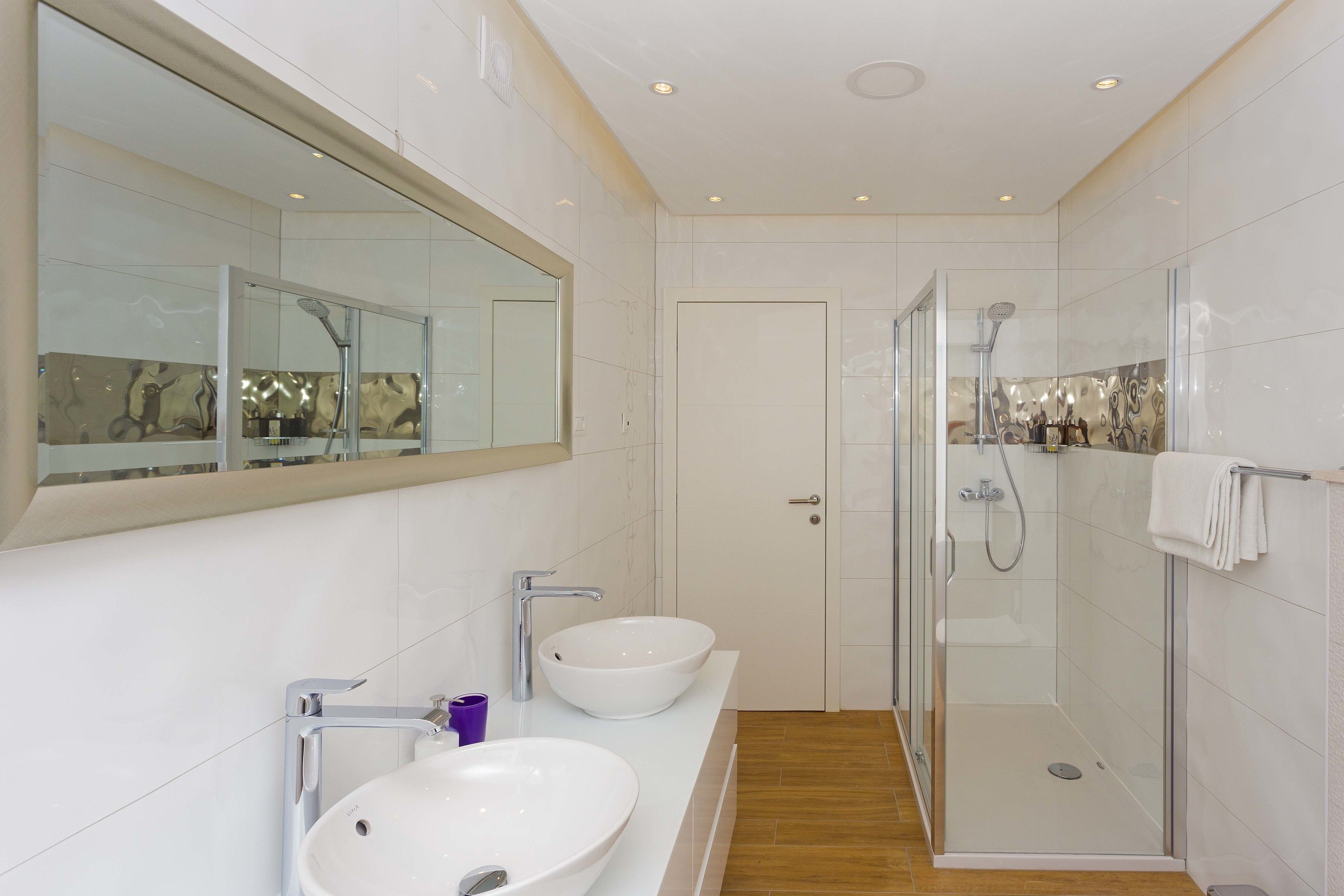 Un baño moderno con dos lavamanos, un espejo grande y una ducha con mampara de vidrio.