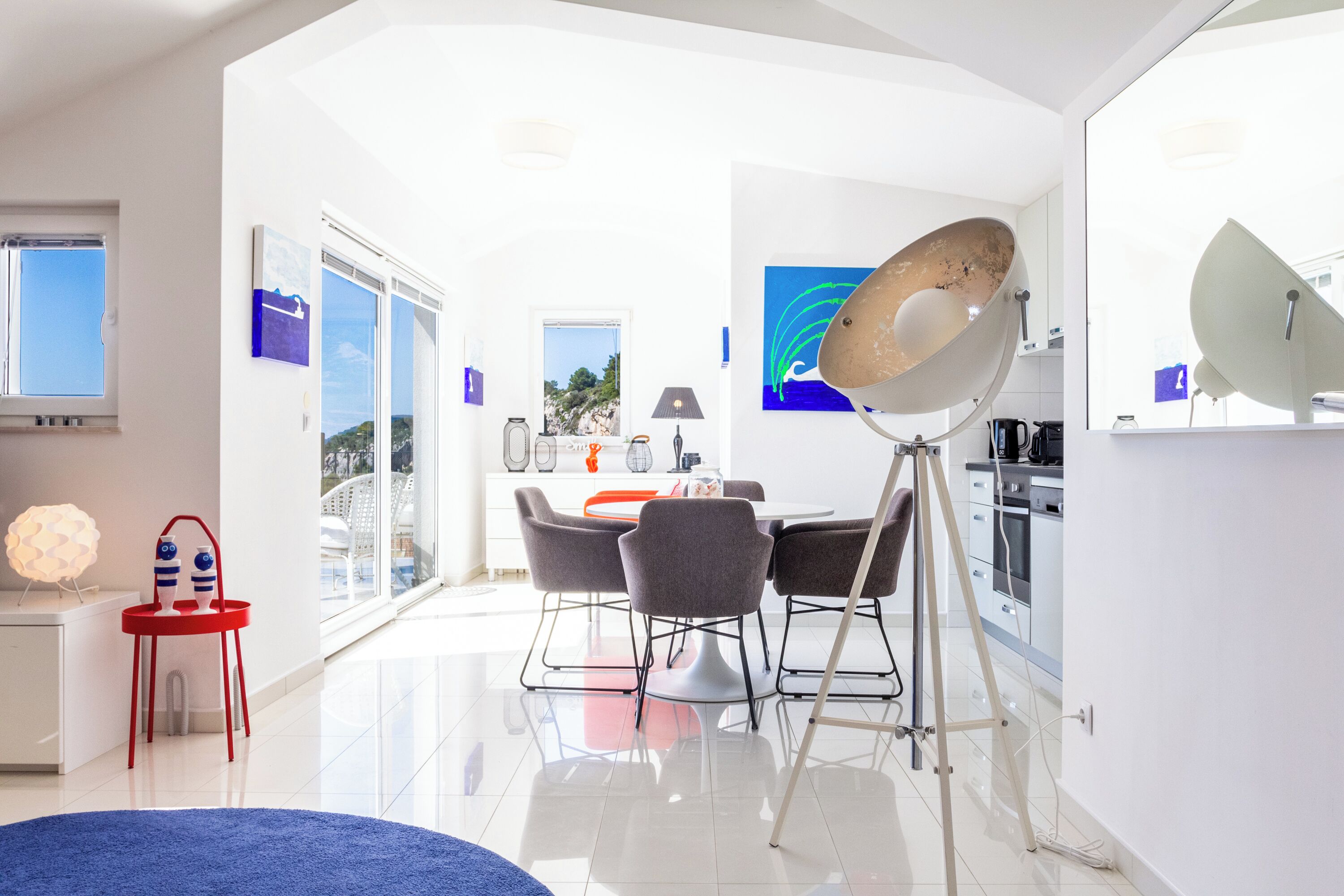 A modern kitchen with white cabinets, a dining area with a round table and chairs, and a large window with a view of the outdoors.