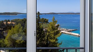 A coastal view through a window, featuring a clear blue sea, a rocky pier, and surrounding greenery. - Blue Bay Residence (Hvar)