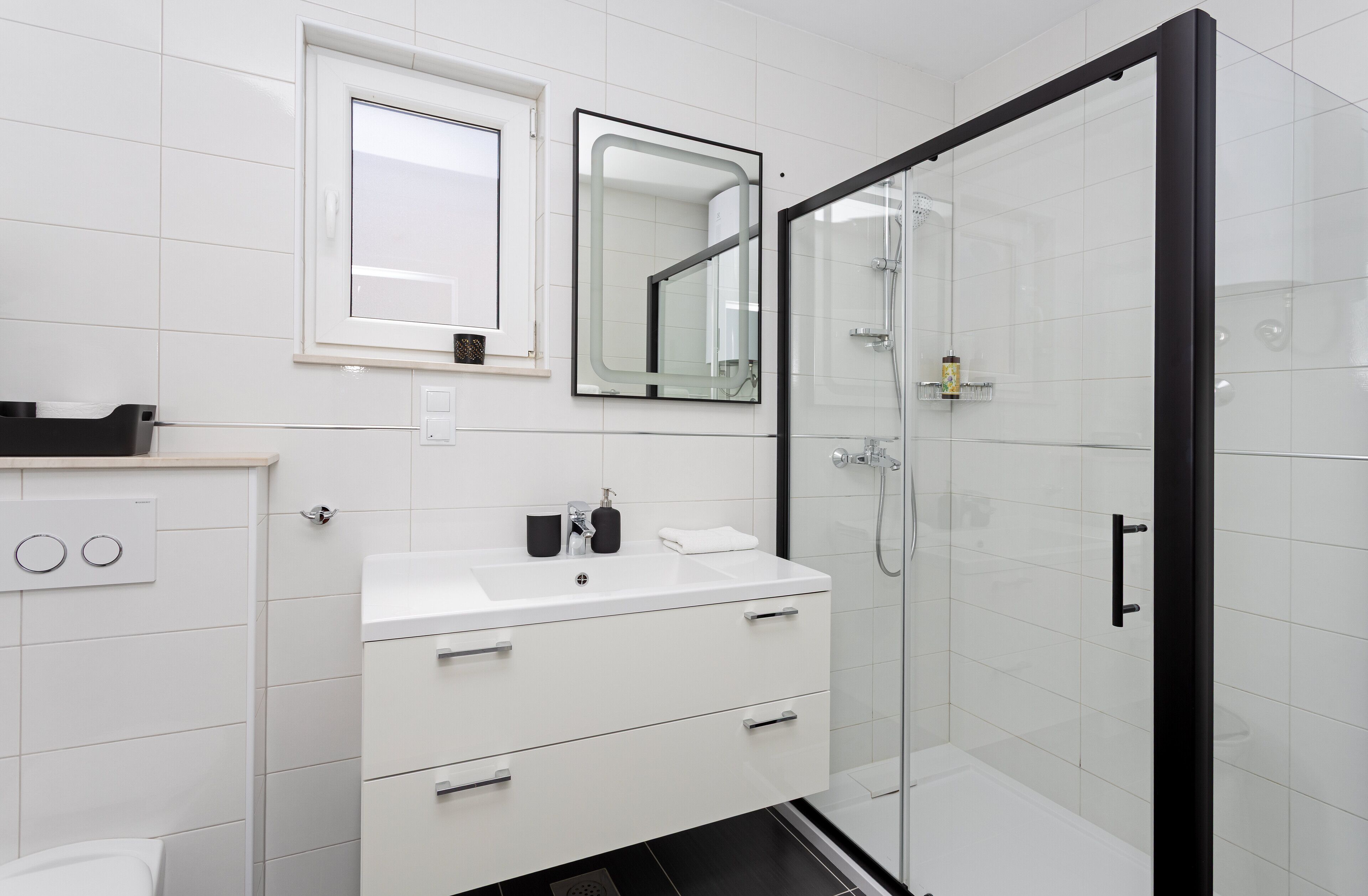 Un baño moderno con un lavabo blanco, dos espejos, una cabina de ducha de vidrio y una puerta negra.
