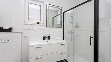 Un baño moderno con un lavabo blanco, dos espejos, una cabina de ducha de vidrio y una puerta negra.