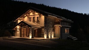 Une grande maison en bois à deux étages, avec un toit en pente, des fondations en pierre et un petit porche.