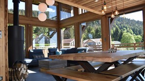 Un intérieur spacieux en bois, doté de grandes fenêtres, d’une cheminée et d’un coin repas.