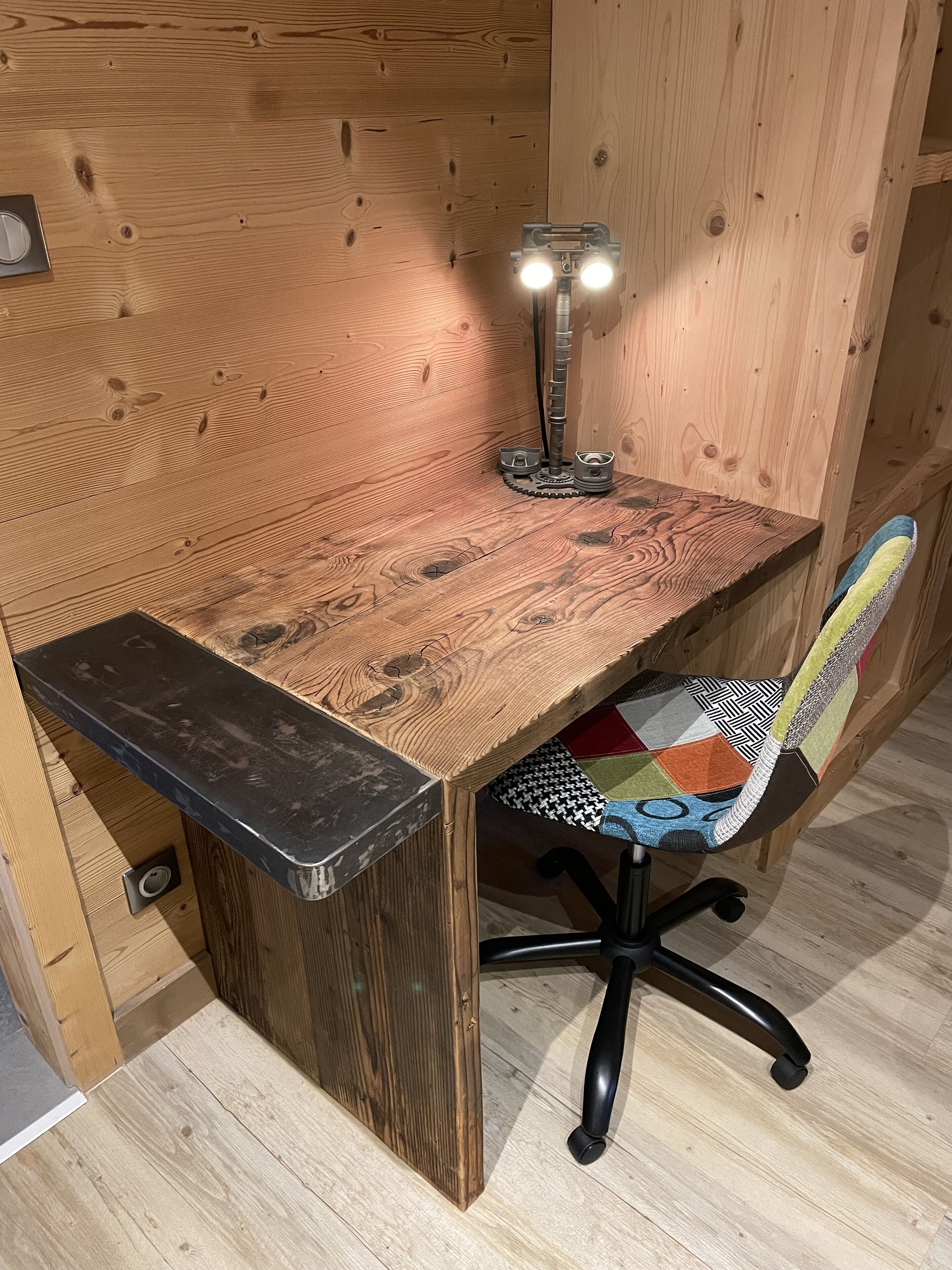Una scrivania in legno con piano nero e una sedia con cuscino colorato.