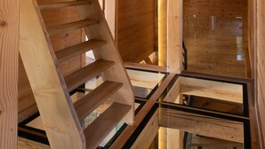 Un escalier en bois, protégé par une paroi de verre, mène à un niveau supérieur où les poutres en bois sont apparentes et où le plafond est en pente.