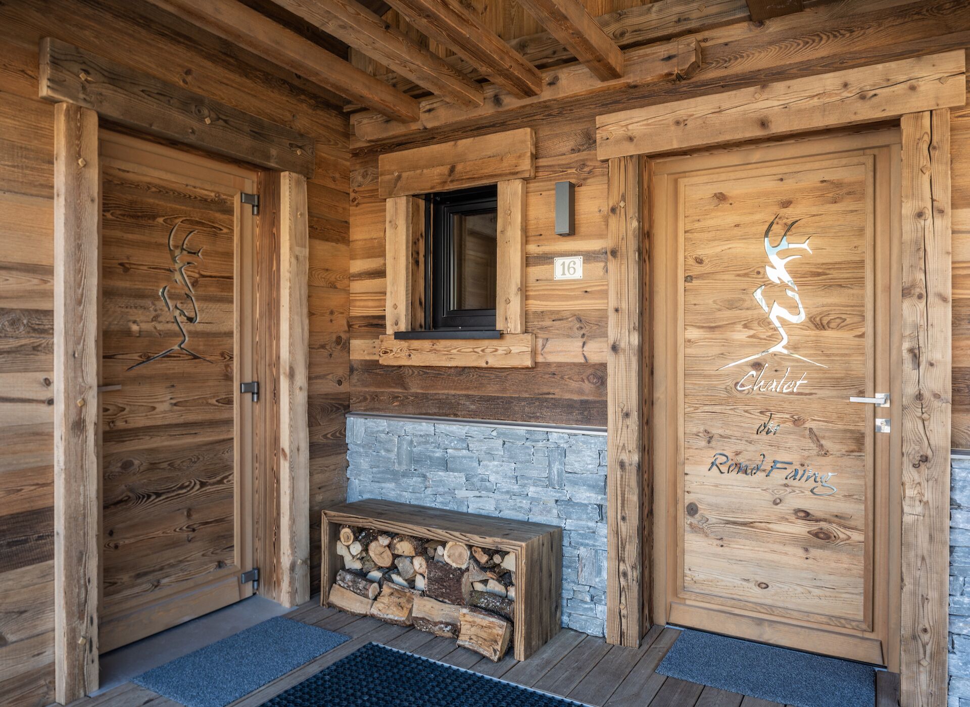 A wooden cabin with a stone fireplace, a bench with firewood, and a door with a deer carving.
