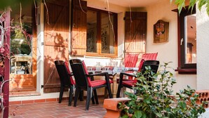 Een terras met een tafel en stoelen, houten luiken en een potplant.