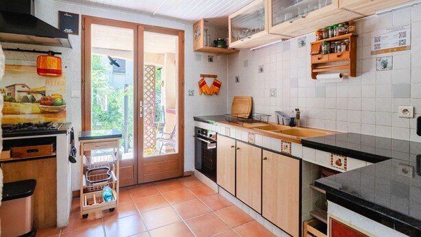 Een keuken met een gasfornuis, houten kastjes, een spoelbak en een raam met uitzicht op een tuin.