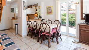 Een eetruimte met een tafel en stoelen, een keuken op de achtergrond en uitzicht naar buiten.