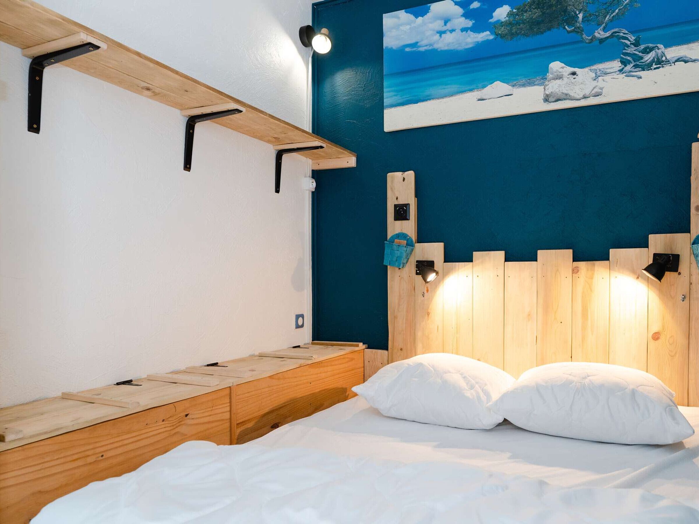Un dormitorio con cabecera de madera, un cuadro de una escena de playa y un banco con una lámpara.
