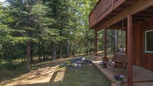 A wooden deck with a bench and potted plants, surrounded by a forested area.