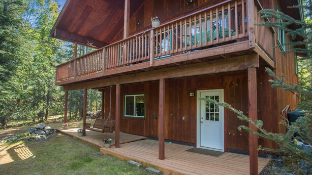 A two-story wooden cabin with a balcony, a front door, and a deck area.