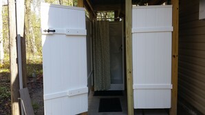 A wooden structure with a door open, revealing a shower area with a floral curtain.