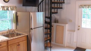 A kitchen with a stainless steel refrigerator, wooden cabinets, a granite countertop, a black spiral staircase, and a door with a window.