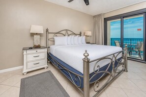 Een slaapkamer met een bed, nachtkastjes, een balkon met uitzicht en een plafondventilator.
