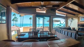Comedor con vista al océano, techo de madera y zona de estar con televisor.