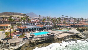 Un resort costero con varias piscinas, palmeras y un litoral rocoso.