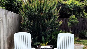 Zwei weiße Adirondack-Stühle auf einer Holzterrasse, in der Mitte ein Blumentopf und eine Laterne.