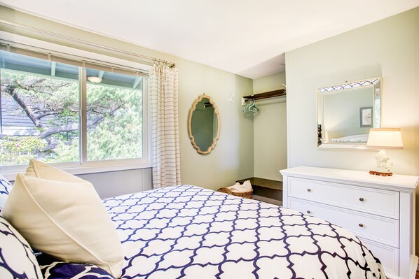 A bedroom with a bed, a dresser, a mirror, and a window with curtains.