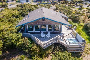 A two-story house with a large deck, a hot tub, and a covered outdoor seating area.