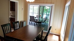 Un coin repas avec une table et des chaises en bois, un ventilateur de plafond et une vue sur l’extérieur grâce à une porte-fenêtre coulissante.