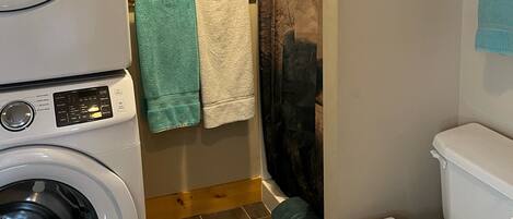 Et lille badeværelse med en forlæder-vaskemaskine, toilet og bruseforhæng.