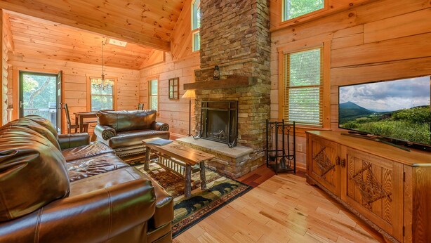 A log cabin interior with a stone fireplace, leather sofa, wooden floors, and a television. - Private Creekside Cabin with Hot Tub (Fleetwood)