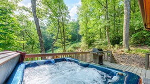 A hot tub surrounded by a wooden deck and a forested area. - Private Creekside Cabin with Hot Tub (Fleetwood)