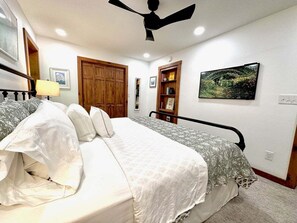 Una camera da letto con un letto, una ventola a soffitto, un armadio in legno, una libreria e un quadro appeso al muro.