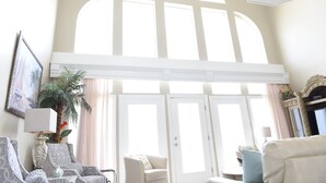 A spacious living room with a high ceiling, large arched windows, and a fireplace.